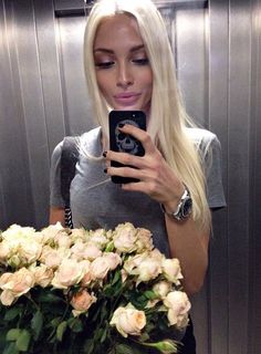 a woman taking a selfie in front of a bunch of flowers with her cell phone