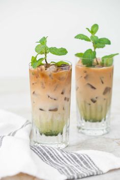 two glasses filled with ice cream and mint sprouts sitting on top of a table