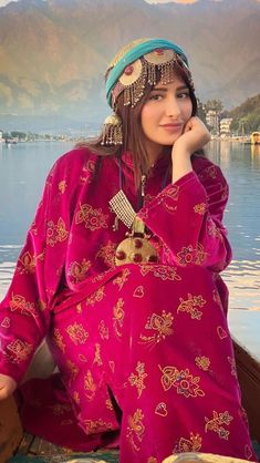 a woman sitting in a boat on the water wearing a headdress and jewelry