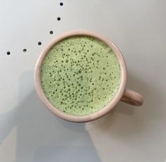 a cup filled with green liquid sitting on top of a white table next to black dots