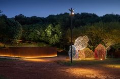 an illuminated sculpture in the middle of a park at night with trees and bushes behind it