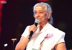 an older woman holding a microphone in front of her face and speaking into the microphone