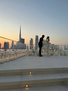 a bride and groom standing on the roof of a building with city lights in the background