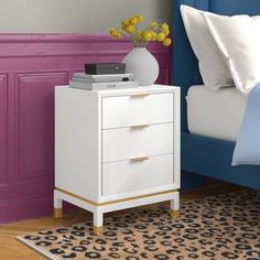 a white nightstand sitting on top of a bed next to a blue headboard and pillows