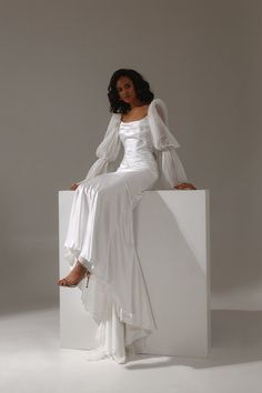 a woman sitting on top of a white box wearing a long sleeved wedding dress