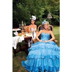 two women dressed in blue dresses sitting at a table with tea and cake on it