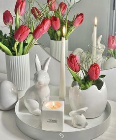 a white tray topped with vases filled with flowers and bunny figurines next to candles