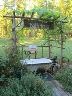 an old bathtub in the middle of a garden with a sign that says bath house