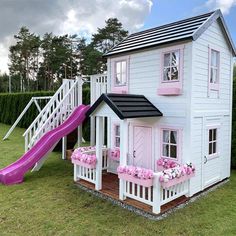 a doll house with a slide and flowers in the window boxes on the front lawn