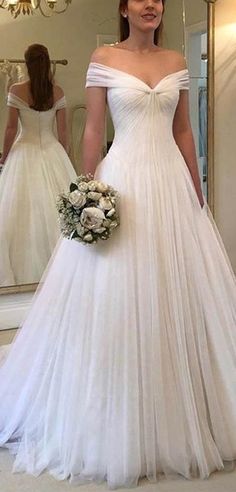 a woman in a white wedding dress standing next to a mirror and holding a bouquet