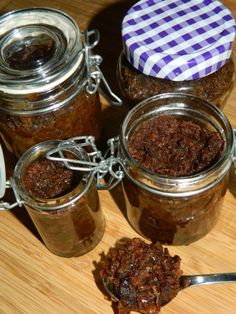 three jars filled with food sitting on top of a wooden table next to a spoon