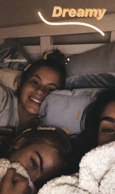 three young women laying in bed under the covers and blankets with their faces close together