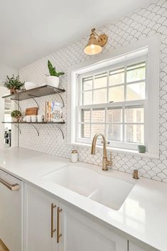 a kitchen with white counter tops and gold faucets on the window sill