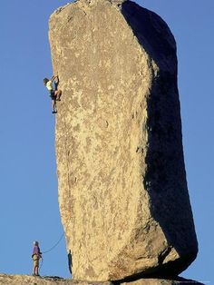 a man climbing up the side of a large rock with a rope attached to it