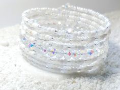 three white beaded bracelets sitting on top of a pile of white carpeted material