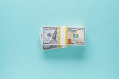 two stacks of one hundred dollar bills sitting on top of each other in front of a blue background