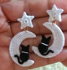 the small black cat is sitting on the crescent moon and star dangle earrings in white crochet