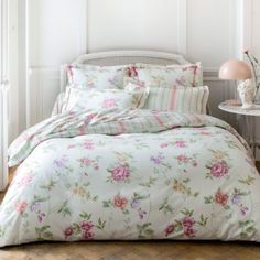 a bed with floral comforter and pillows in a room next to a lamp on a table