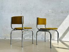 two yellow chairs sitting next to each other in front of a white wall and cement floor