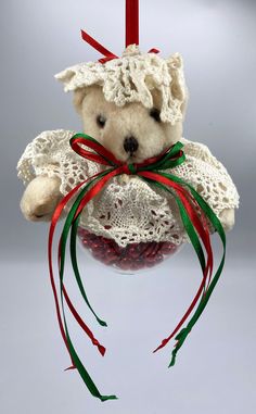 a white teddy bear hanging from a red and green christmas ornament with ribbon