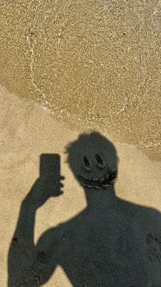 a shadow of a man holding a cell phone on the sand near the water's edge