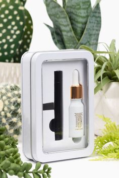 an open white box with some plants in it and a small bottle next to it