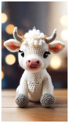 a small crocheted cow sitting on top of a wooden table with lights in the background