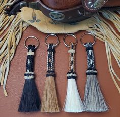 four tasseled keychains are sitting on a brown leather surface next to a cowboy hat