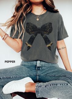 Description: Discover the charm of our Comfort Colors Coquette Bow Butterfly Shirt, featuring a delicate cicada bow design. This black coquette tee is the perfect trendy moth ribbon oversized t-shirt for spring, making it a delightful gift for mom. Enjoy both style and comfort with this unique and fashionable piece. AI Generated Art with post editing and touch up. 🦋 Premium Comfort Colors Fabric: Ensures a soft and durable wear that feels great on the skin. 🦗 Unique Design: Showcases a chic co Casual Black Top With Bow, Mott And Bow T Shirt, Spring Crew Neck T-shirt With Bow, Spring Cotton T-shirt With Bow, Casual T-shirt With Bow Print And Crew Neck, Cute Cotton T-shirt With Pink Bow, Spring T Shirts, Butterfly Shirts, Bow Design