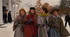 three women dressed in period clothing are walking through the snow with their hands on their hips