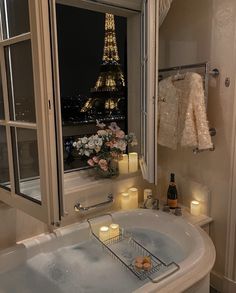 a bath tub sitting next to a window with candles in front of the eiffel tower