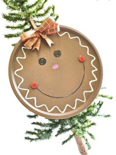 a paper plate with a face on it hanging from a christmas tree branch in front of a white background