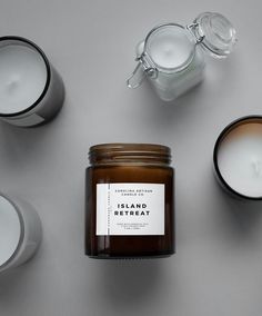 candles and jars with labels on them sitting next to each other in front of a gray background