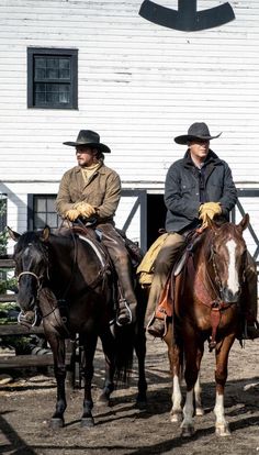 two men riding horses in front of a white building