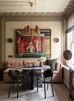 a dining room table with chairs and a painting on the wall above it, in front of a couch