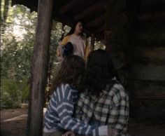 two people sitting under a wooden structure in the woods