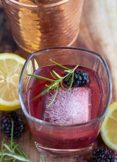 a glass filled with liquid next to sliced lemons and blackberries