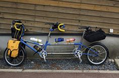 a blue bike parked next to a wall with two backpacks on it's back