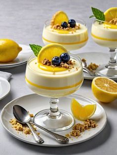 three desserts with lemon and blueberries are on white plates next to silverware