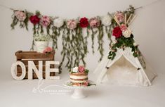 there is a cake on the table next to a teepee with flowers and greenery