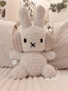 a white stuffed rabbit with headphones on it's ears sitting on a bed