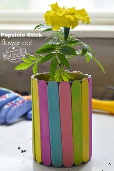 a flower pot made out of popsicle sticks with a yellow flower in the center