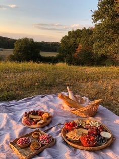 two baskets filled with food sitting on top of a white blanket next to a field