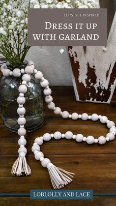 a white beaded necklace sitting on top of a wooden table next to a vase with flowers