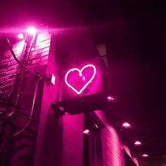 a neon heart sign on the side of a building with lights around it and a fire escape in the background