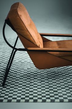 a brown leather chair sitting on top of a checkered floor next to a black metal frame