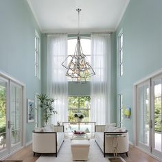 a living room filled with furniture and a chandelier hanging from the ceiling in front of two windows