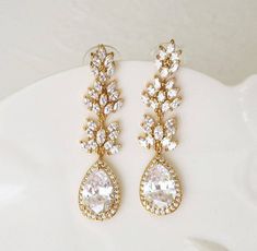 two pairs of gold tone earrings with white stones and clear crystal tears, on a white plate