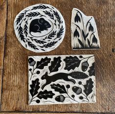 three pieces of pottery sitting on top of a wooden table with leaves and animals painted on them