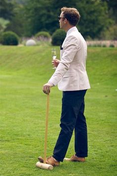 a man in a suit holding a wine glass and standing on the grass with a cane